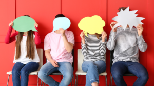 4 young people sat against a red background holding paper speech bubbles over their faces